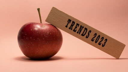 Trends 2023 lettering on wooden surface. Apple pink background concept.