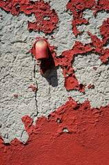 Dettaglio del muro di una casa con l'intonaco rosso scrostato e rovinato da cui esce un tubo