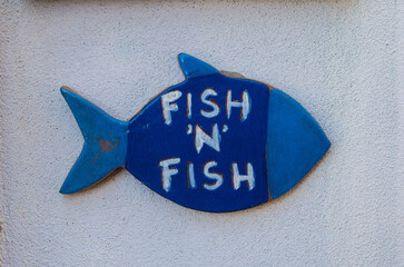 Un pesce di legno verniciato di blu e con la scritta fish and fish appeso a un muro di una casa di...