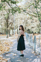 middle-aged woman in autumn felt hat and a bouquet of maple leaves walk in the park in the fall season, brown autumn tones