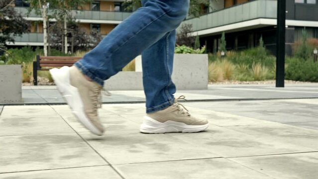Women's legs in sneakers and jeans walk along the pavement, paved with light-colored tiles. City street in early autumn.