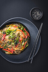 Japchae or  Chapchae in black bowl on the dark table. Korean cuisine glass chapchae noodles dish with vegetables and sesame. Asian traditional food. Authentic meal