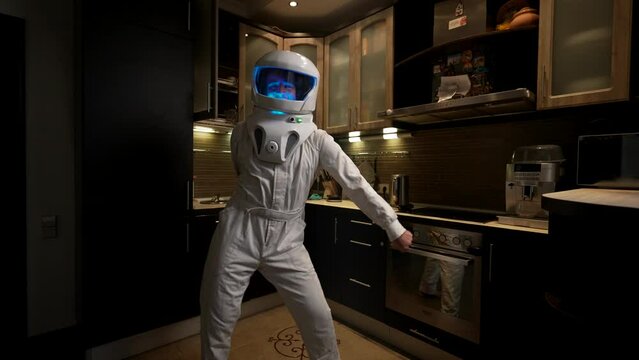An astronaut in the interior of the kitchen dances a famous dance. White astronaut costume, with blue backlight. Favorite work concept