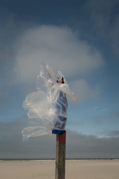 abstract art portrait of woman in long blue dress on beach pole with white plastic sheet, sky and cloud