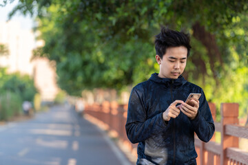Fototapeta premium Asian sportsman is using mobile phone outdoors.
