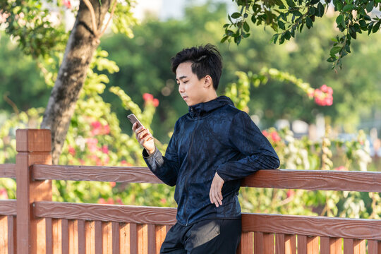 Asian sportsman is using mobile phone outdoors.