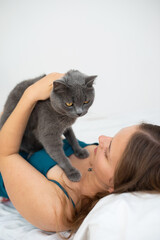 Pretty young woman playing with her British shorthair cat in her bed