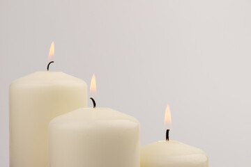Burning white wax candles on white background.