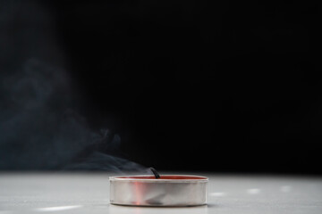 A extinguished candle emitting smoke standing on the table, a black background. Soft selective focus