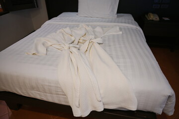 Close-up of two white bathrobes stacked on a single bed in a hotel room. The robe was placed on the bed in the room.
