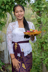 Women wear traditional Balinese kebaya in a green garden holding god's offerings
