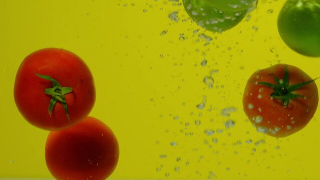 Cinematic shot of small red tomatoes falling and splashing into the cold fresh water.Ripe Apples Falling Through Water. 4k shoot