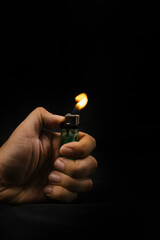 Close up a lighter with a flame in a man's hand on dark background. Smoking and insurance and arson...