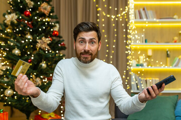 Dissatisfied and disappointed man looking at camera nervously trying to do online shopping while...