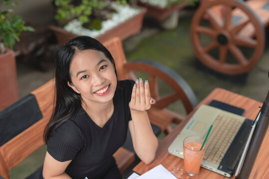 A smiling Southeast Asian teenage girl flexes her black and white fire design nail extensions to the camera