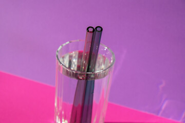 Reusable glass Straws in Glass with water on purple violet background Eco-Friendly Drinking Straw...