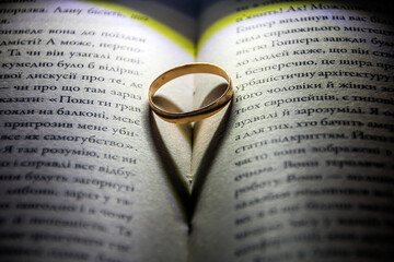 An engagement gold ring lies between the pages of a book and casts a heart-shaped shadow 