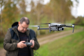 Mature man operating drone flying or hovering by remote control in nature