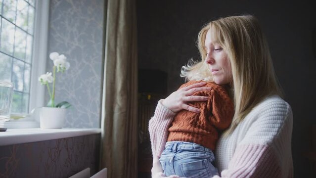 Unhappy mother cuddling young son at home sitting next to radiator during cost of living energy crisis - shot in slow motion