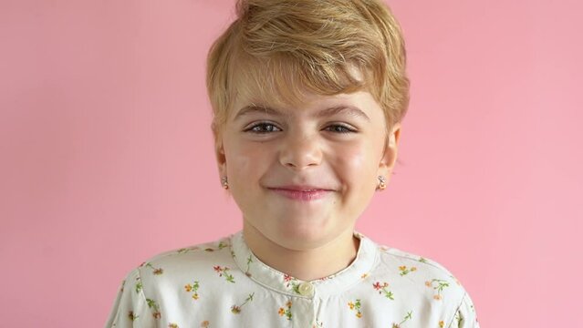Portrait of surprised and happy satisfied child preschool girl in light casual dress looking at camera over pink background. Positive mood conception children products holidays advertising.