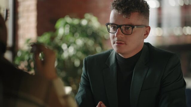 Man with glasses conducts negotiations talks and conducts a job interview or discusses issues with a woman sitting at a table. Business meeting of a man and a woman, a dialogue between two partners