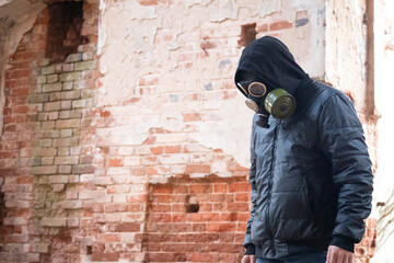 Fototapeta na wymiar A guy in a gas mask stands against a brick wall and stares at the ground. A sad look in the photo
