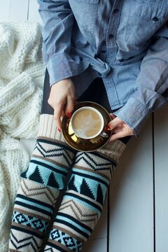 A cup of hot cappuccino coffee on the girl's lap. Warm clothes, cold season.