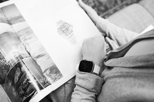 London, United Kingdom - Sept 28, 2022: Monochrome image fashionable woman reading advertising inside Watch your Time by Le Monde nespaper wearing new Apple Watch Ultra