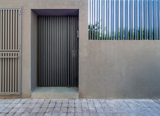 A modern house entrance, with a grey door and fence wall by the sidewalk. Athens, Greece.