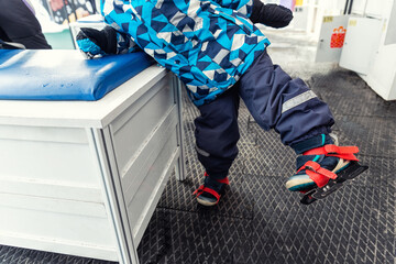 Close-up detail view of little kids leg wearing blue plastic rental skating boots standing on non-slip rubber soft mat in dressing room of skating rink. Healthy children recreation leisure activity