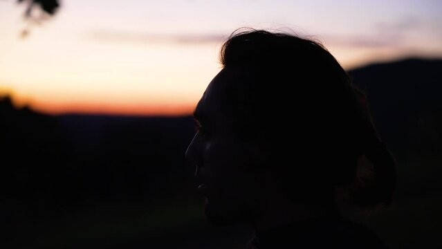 Close up of a head of a young man in front of mountains and a beautiful orange sundown.