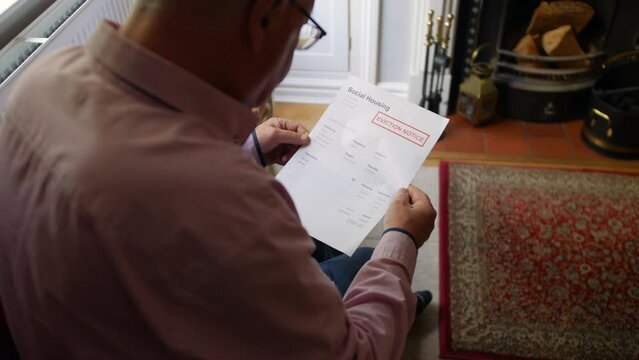 A lonely senior man opening a debt letter. The mature male is reading a social housing eviction notice at home