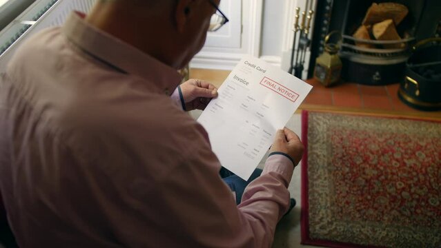 A lonely senior man opening a debt letter. The mature male is reading a credit card bill final notice at home
