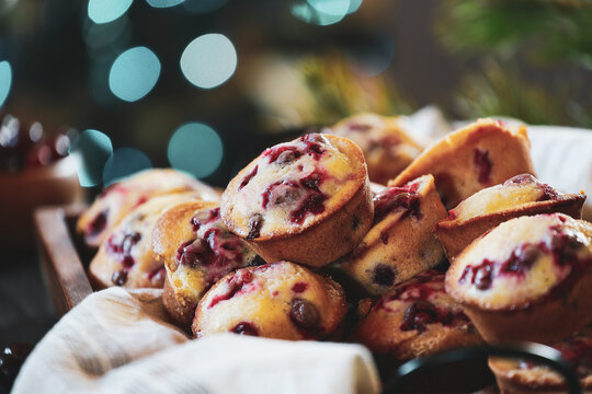 Cranberry muffins in a wooden tray with Christmas tree bokeh and fresh berries in the background. Extreme selective focus with blurred foreground and background.