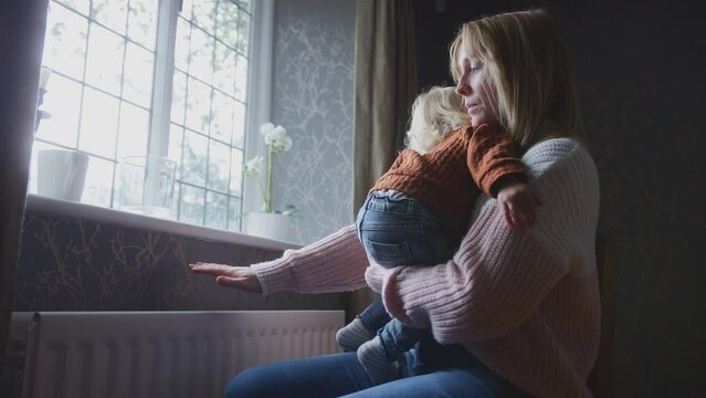 Unhappy mother cuddling young son at home sitting next to radiator during cost of living energy crisis - shot in slow motion