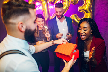 Multiracial couple exchanging gifts for birthday party or new years eve in the club