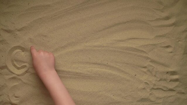 the child writes a word on the sand with his finger. the word chuffed. slow motion video