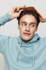 Close-up photo. a handsome young man combs his hair in a light light blue hoodie,with a comb in his hand combing a place in the background for inserting an advertising layout.Vertical portrait photo .