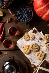 Cookies in the shape of pumpkins and ghosts are in a plate on the table. Next to a teapot and mugs, an autumn still life