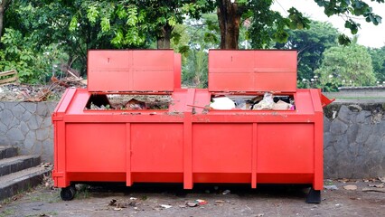 Metal durable orange industrial trash bin for outdoor trash at construction site. Large waste basket for household or industrial waste. A pile of waste