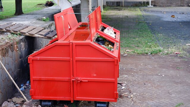 Metal durable orange industrial trash bin for outdoor trash at construction site. Large waste basket for household or industrial waste. A pile of waste