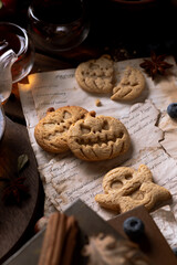 Cookies in the shape of pumpkins and ghosts are in a plate on the table. Next to a teapot and mugs, an autumn still life