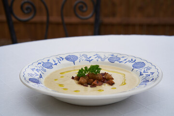 Close up picture of the bowl or deep plate full of creamy celery root soup with bread crumbs, parsley and drops of extra virgin olive oil served outside on the table of garden restaurant. Healty dish.