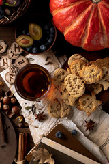 Cookies in the shape of pumpkins and ghosts are in a plate on the table. Next to a teapot and mugs, an autumn still life