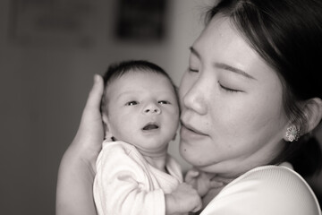 artistic black and white lifestyle shot on young and happy Asian Chinese woman holding adorable newborn baby girl in her arms in mother and daughter love concept