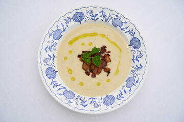 Top view closeup picture of isolated deep rustic plate with delicious traditional creamy celery root soup served with bread crumbs, parsley and extra virgin olive oil. Healty dish full of nutritions.