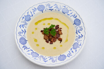 Delicious creamy celery soup with roasted bread crumbs and sprinkled by extra virgin olive oil served in vintage blue onion porcelain plate. Delicate seasonal vegetarian dish cooked mainly in winter.