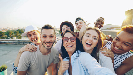 Point of view shot of happy friends taking selfe on roof at summer party laughing, posing and...