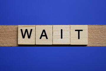 word wait made from wooden gray letters lies on a blue background