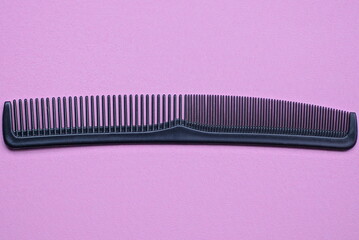 one long black plastic comb lies on a pink table